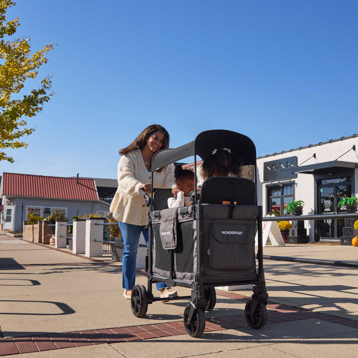 happy mom pushing two kids in a W2 Elite Pro Charcoal Gray Stroller in an outdoor setting